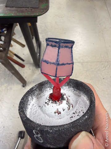 The wax model of the vase. It has a hexagonal base, rectangular sides up to 1/3 of the way up, then tapers in a bit before flaring out to form a lip. It's held to the flask base with three wax sprues. Most of the vase is pink sheet wax, but the joins are ropy blue